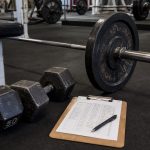 Gym floor with dumbbells, barbell, and training log for a hypertrophy rep range guide