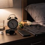 Nightstand with alarm clock, sleep tracker, water, gym clothes, and meal prep container