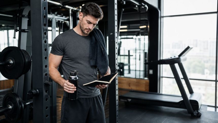 Lifter reviewing a workout notebook beside a barbell rack and treadmill for exercise and weight loss planning