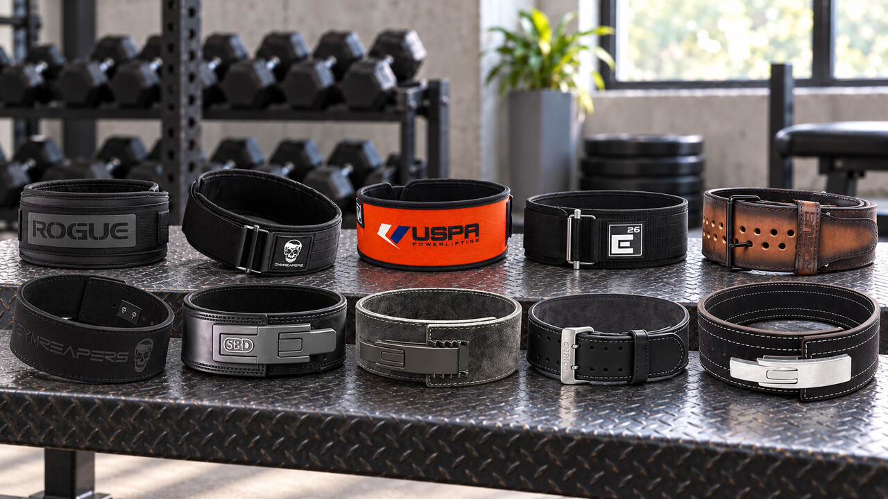 Ten nylon, leather prong, and lever weightlifting belts arranged on a gym bench
