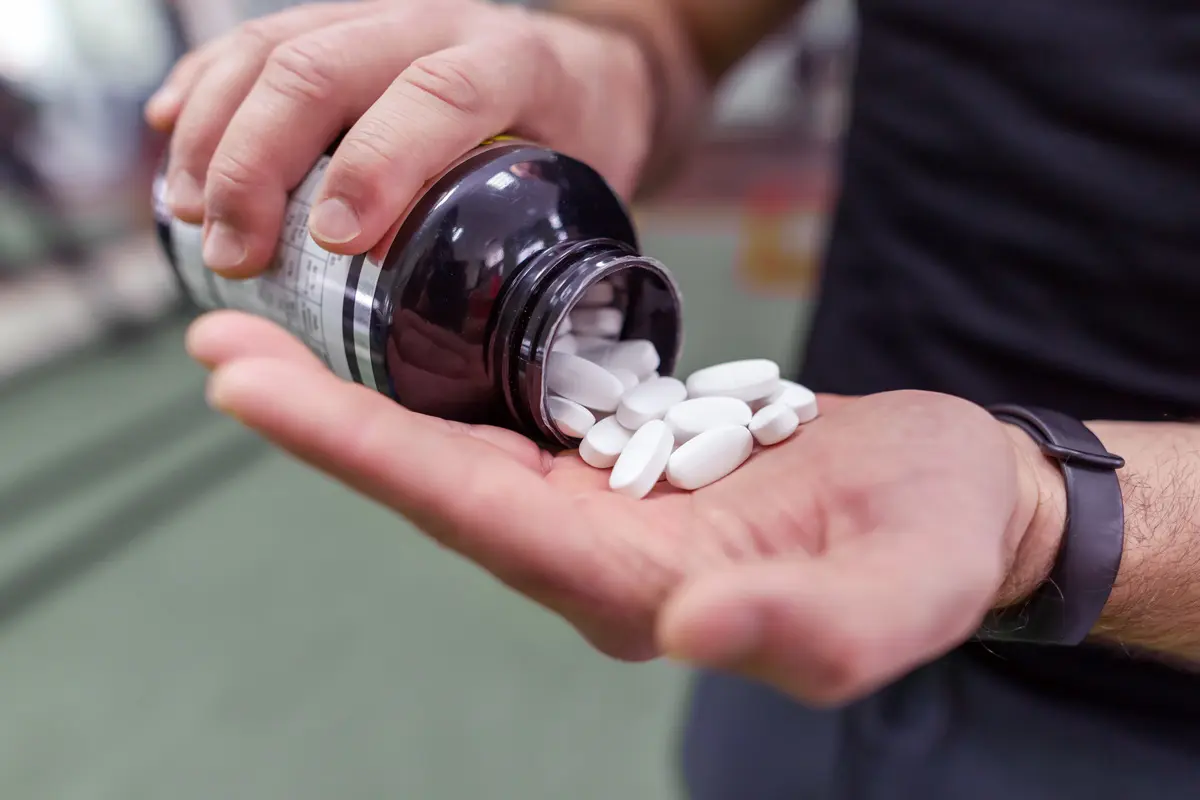 Person pouring white supplement tablets from a bottle into their hand