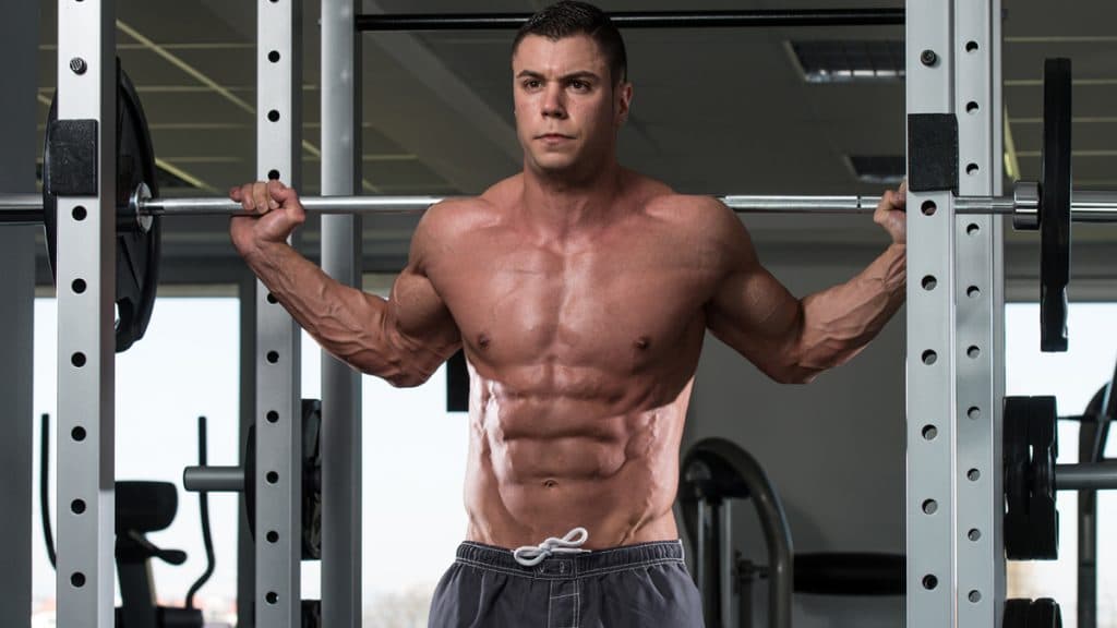 Muscular lifter holding a barbell across the upper back in a squat rack