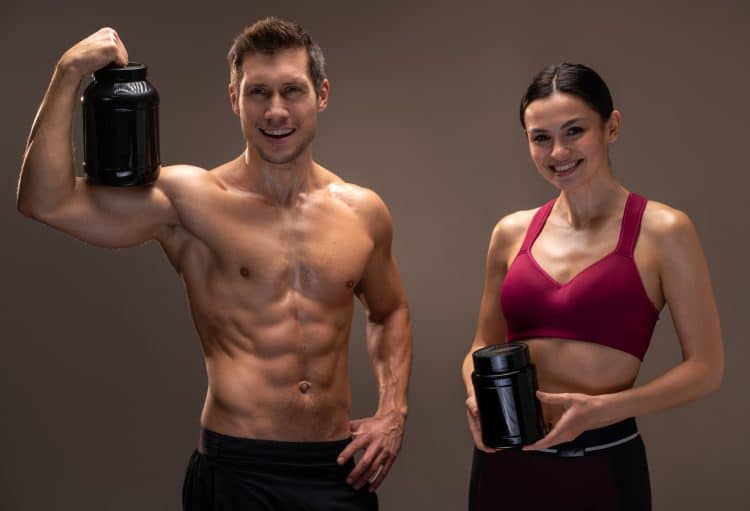 Muscular Male And Female Holding Supplements