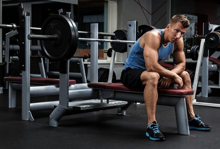 Lifter seated beside a racked barbell on a flat bench