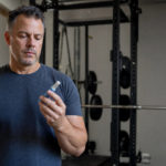 Adult holding a GLP-1 injector pen in a home gym setting, illustrating the protocol to keep muscle while taking GLP-1 weight-loss drugs