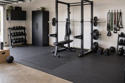 Organized home gym with clear lifting space, rubber flooring, rack, dumbbells, and safe storage