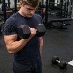 Lifter performing a strict dumbbell curl with a training log nearby