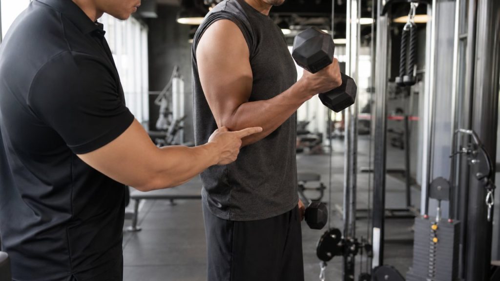 Coach observing dumbbell curl elbow position during biceps and triceps training
