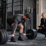 Coach observing a conventional deadlift setup with a loaded barbell in a strength gym