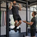 Coach supervising a lifter performing a strict pull-up on a straight gym bar