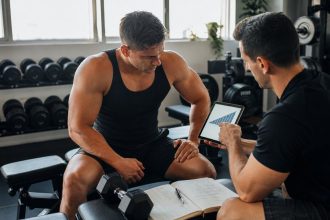Coach reviewing hypertrophy training progress with a lifter in a modern gym