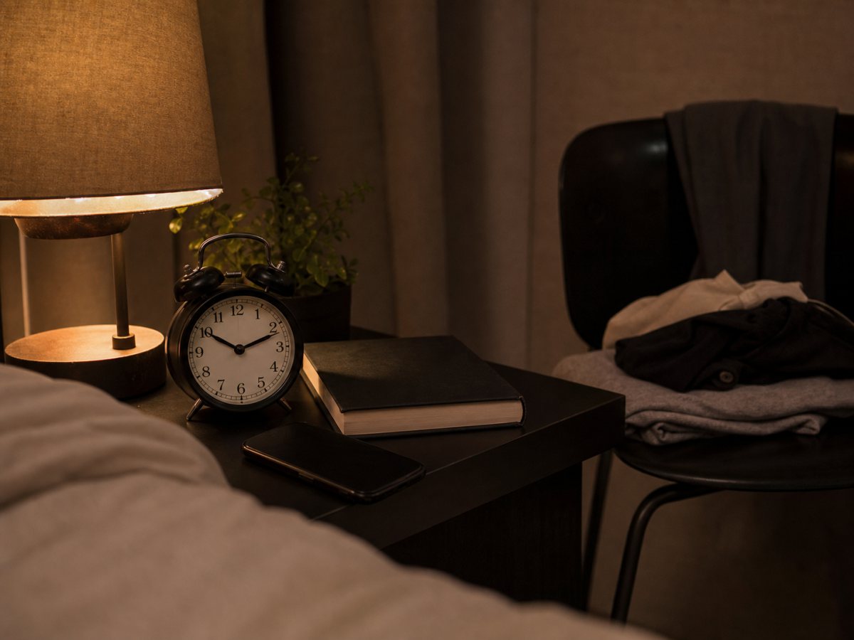 Nightstand with alarm clock, book, lamp, and phone away from the bed