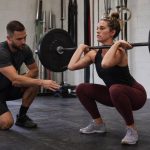 Coach guiding a lifter through controlled front squat practice in a gym