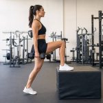 Woman performing a dumbbell step-up with one foot planted on a padded box