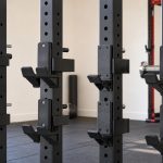 Padded power rack J-hooks mounted on square steel uprights beside a barbell