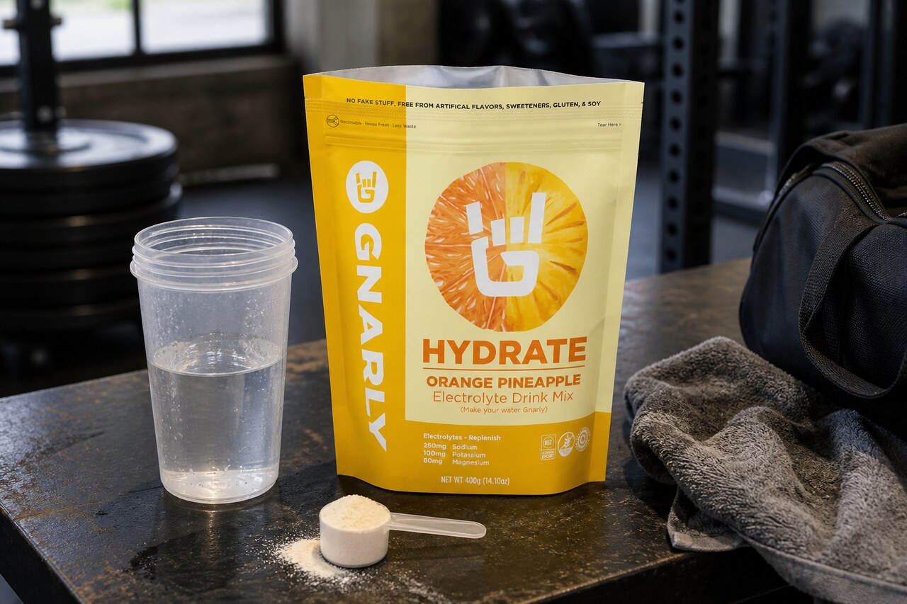 Gnarly Hydrate pouch beside a scoop, shaker, towel, and gym bag in a mixing setup
