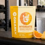 Gnarly Hydrate Orange Pineapple pouch beside a shaker in a gym