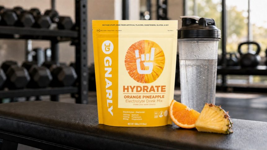 Gnarly Hydrate Orange Pineapple pouch beside a shaker in a gym