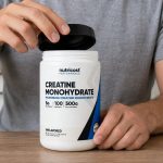 Nutricost creatine tub being opened beside a water bottle