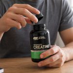 Optimum Nutrition creatine capsules bottle being opened beside water