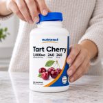 Hands opening a Nutricost Tart Cherry bottle on a kitchen counter