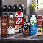 Ten chocolate protein drink containers arranged on a gym bench with brand labels facing forward