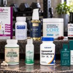 Ten liposomal glutathione supplement packages arranged on a metal workout bench.
