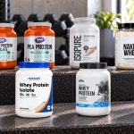 Eight low-carb protein powder packages arranged on a gym bench with their front labels visible
