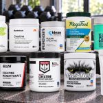 Ten unflavored creatine powder packages with visible brand labels on a gym bench