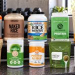 Ten soy, rice, hemp and pumpkin protein packages with labels facing forward on a gym bench
