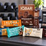 Eight protein bar varieties with readable wrappers and an IQBAR box arranged on a gym bench