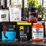 Eight selected protein powder packages on a gym bench, including unflavored whey, pea protein and chocolate isolates
